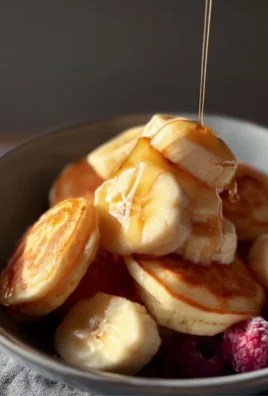 A stack of fluffy mini banana pancakes topped with fresh bananas and syrup.