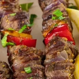 Grilled lamb kabobs garnished with vegetables on a wooden plate