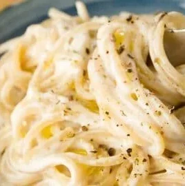 Cream cheese pasta dish garnished with herbs and served in a white bowl