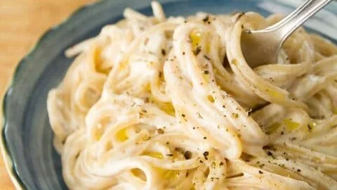 Cream cheese pasta dish garnished with herbs and served in a white bowl