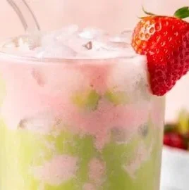 Iced strawberry matcha tea latte served in a glass with strawberries and matcha powder.