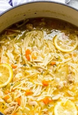 Bowl of homemade lemon chicken noodle soup garnished with herbs.