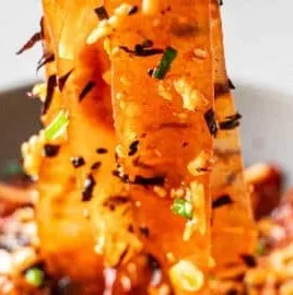 Bowl of spicy glass noodles topped with Buldak hot sauce and fresh vegetables